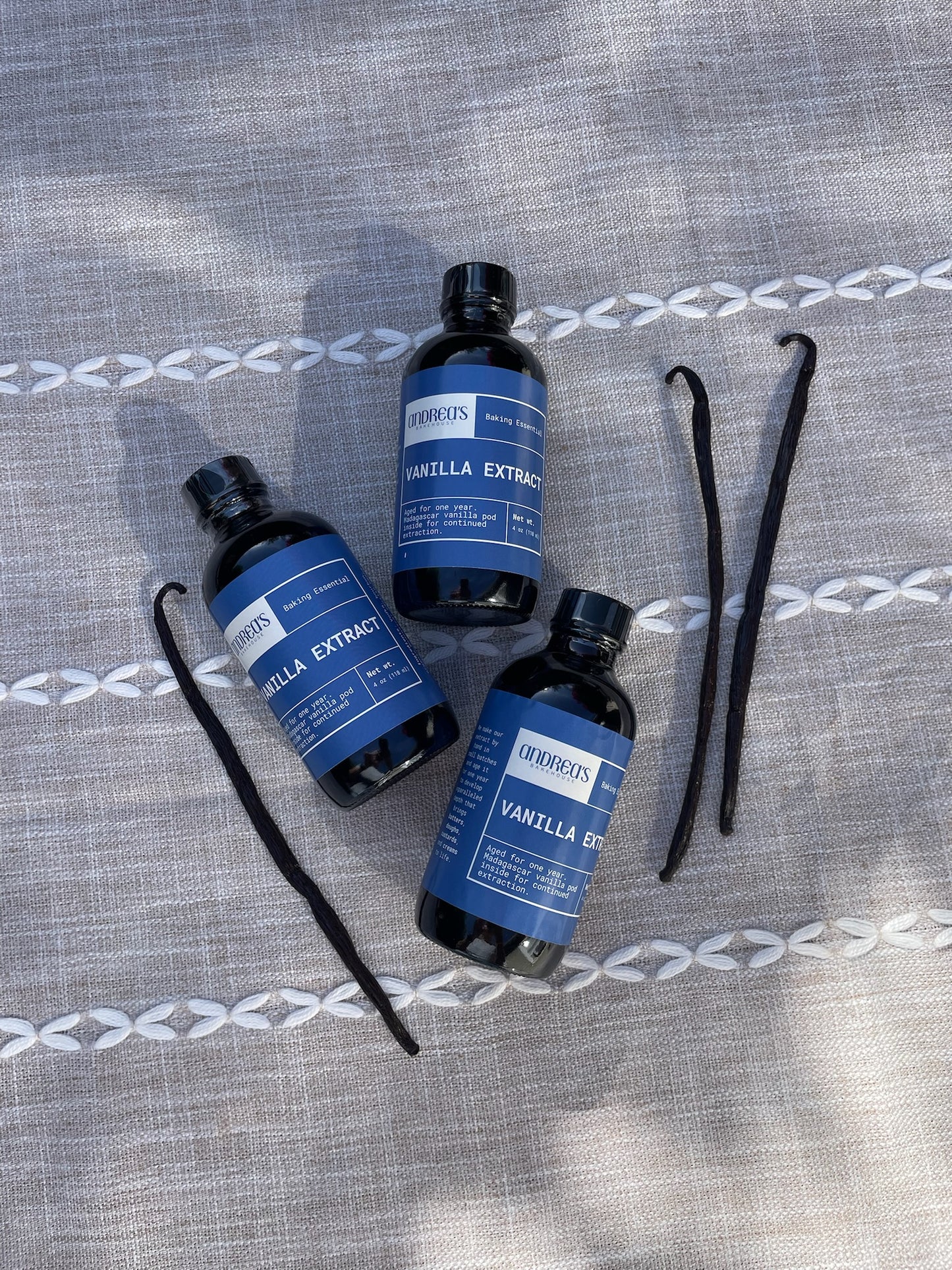 Handmade aged vanilla extract with blue labels on a textured gray surface.